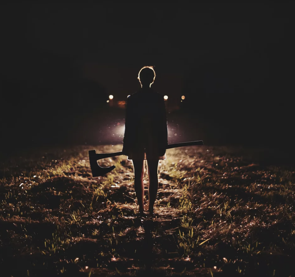A silhouetted figure holding an axe in a dark field at night